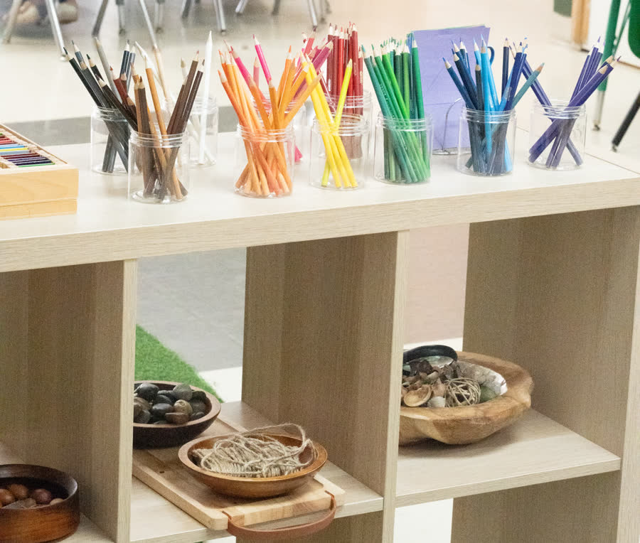 Des pots de crayons de couleur et des bols de matériaux naturels sur une étagère basse