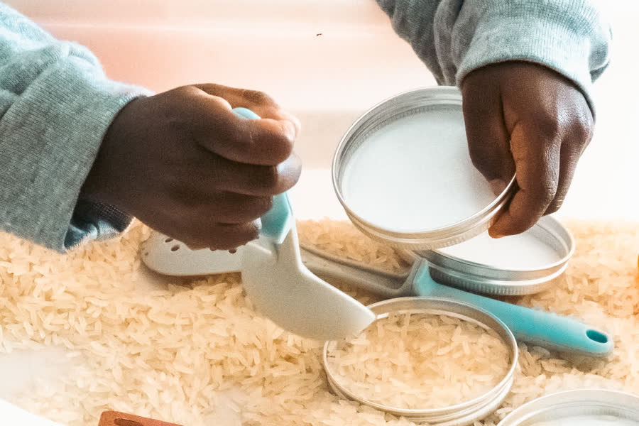 Des mains transvasent du riz à la table sensorielle